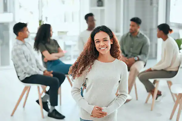 Smiling woman standing in front of a diverse group seated in a bright, modern office.