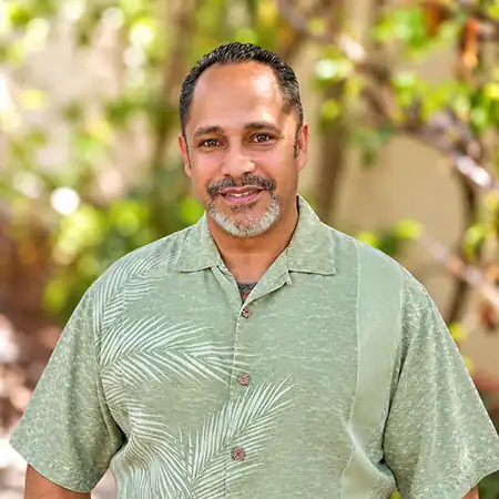 Adam Figeroa - Right Path Recovery San Diego - Right Path Recovery San Diego Smiling man with short gray beard wearing a light green Hawaiian-style shirt, standing outdoors with greenery in the background.