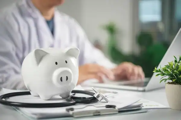 White piggy bank with a stethoscope on papers at a doctor's desk, symbolizing medical savings and budgeting in healthcare