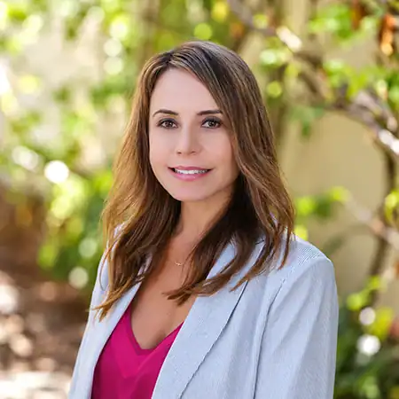 Alyson Albano - Right Path Recovery San Diego - Right Path Recovery San Diego Woman smiling outdoors in a light blue blazer and pink blouse, with greenery in the background.