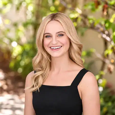 Catherine Mann - Right Path Recovery San Diego - Right Path Recovery San Diego Smiling woman with blonde hair in a black sleeveless dress, outdoors with greenery in the background.