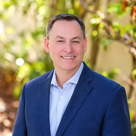 John Peloquin - Right Path Recovery San Diego - Right Path Recovery San Diego Professional headshot of a smiling man in a blue blazer outdoors with greenery in the background