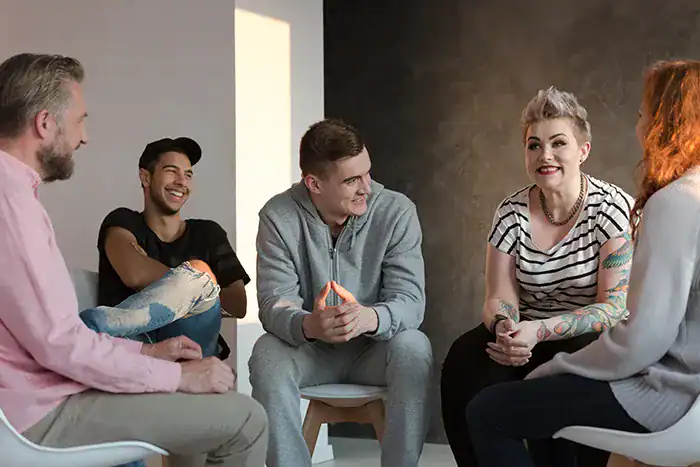 A group of five people seated in a circle, chatting and smiling in a bright, modern room.