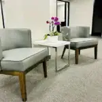 Right_Path_RecoveryRio_IOP10 - Right Path Recovery San Diego - Right Path Recovery San Diego Two gray upholstered lounge chairs with wooden legs flanking a small white table holding a potted orchid in an office waiting area.