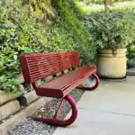 Right_Path_RecoveryRio_IOP35 - Right Path Recovery San Diego - Right Path Recovery San Diego Red slatted metal bench on a concrete path beside a green hedge and a large potted plant in a garden setting.
